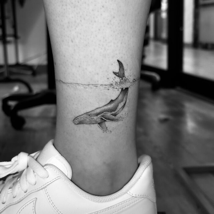 Whale tattoo on ankle with water surface detail, an example of the best tattoos that had everyone hitting the like button.