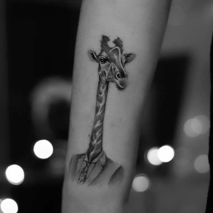 Realistic giraffe tattoo wearing a suit on forearm, showcasing one of the best tattoos with detailed black and gray shading.