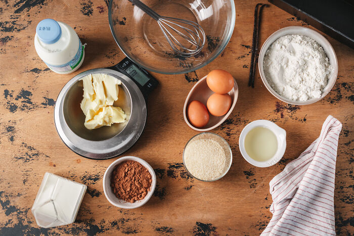 Baking ingredients including eggs, flour, butter, cocoa powder, and milk on a wooden table for childhood cake recipe. - 6
