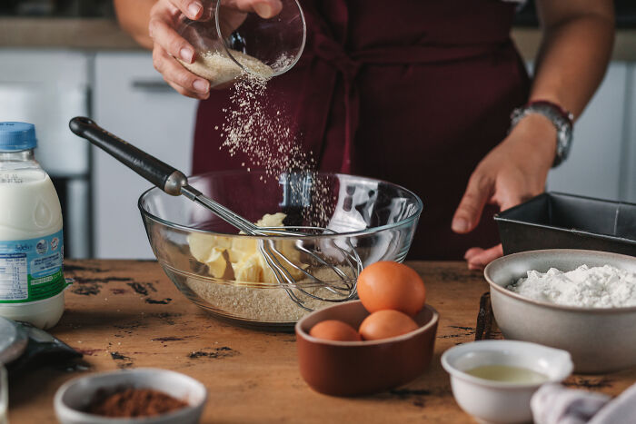 Person pouring sugar into a bowl with butter and whisk, preparing ingredients to bake a childhood cake recipe. - 7