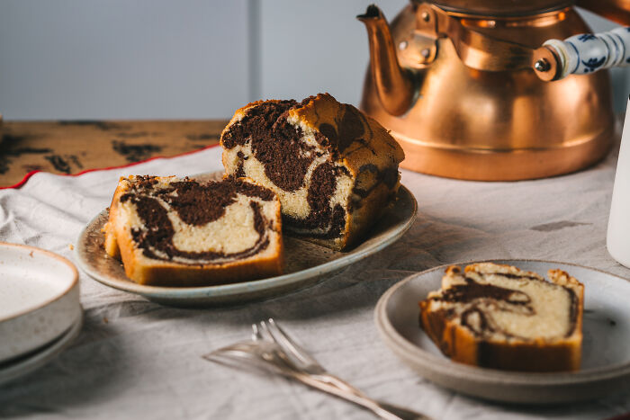 Marble childhood cake sliced on plates next to vintage teapot, symbolizing family remedy after hospital trip. - 1