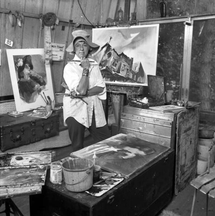 Woman artist in Florida studio painting and breaking barriers in the 1970s, surrounded by her artwork and art supplies.