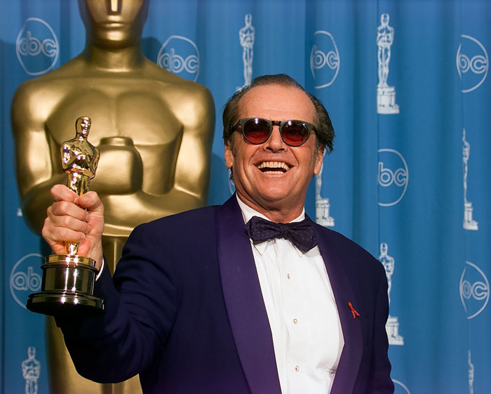 Danny DeVito smiling and wearing sunglasses, addressing fan concerns about Jack Nicholson&rsquo;s health in a formal setting.