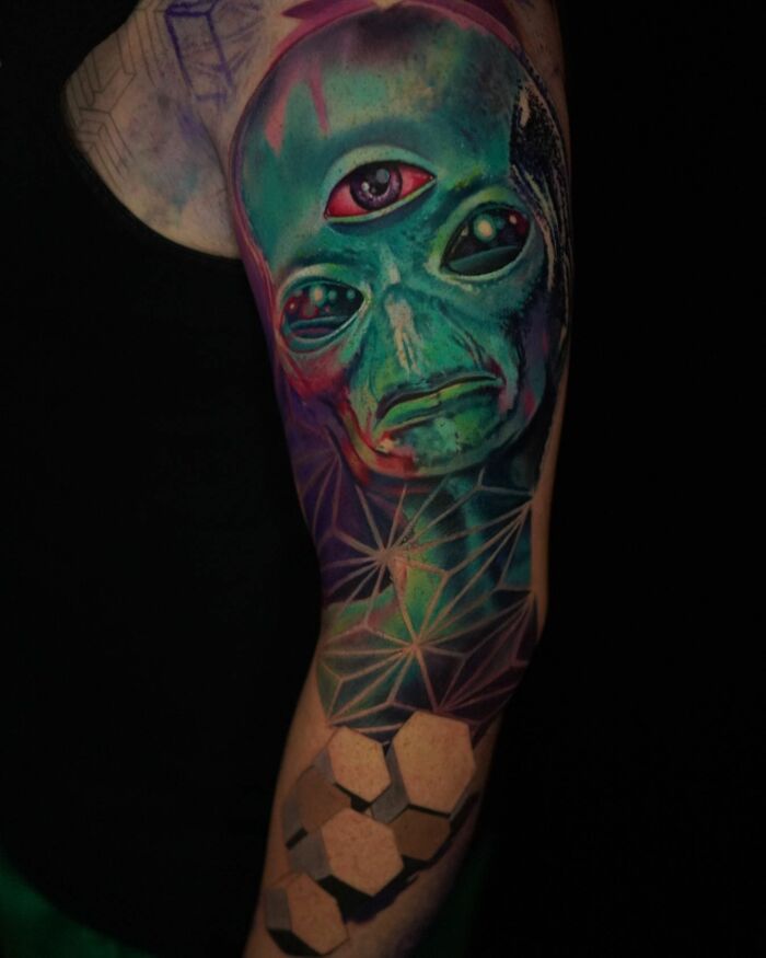 3D tattoo of a green alien with three eyes and geometric shapes, showcasing immersive portal-like body art by Jesse Rix