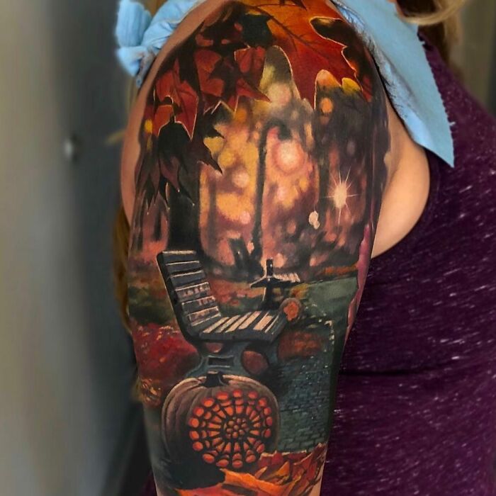 3D tattoo of a park bench with autumn leaves and glowing lights creating a portal to another world effect on upper arm.