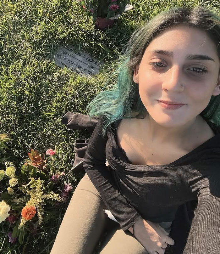 Young woman with green hair sitting on grass near a grave, relating to 7-Eleven employee update after tragic passing.