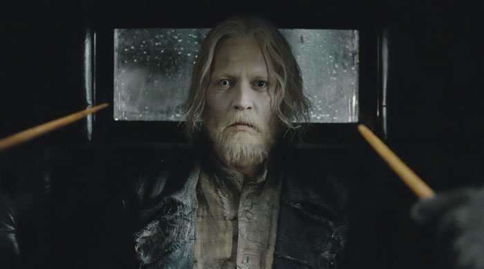Johnny Depp as a weathered character holding wands in a dark setting related to Fantastic Beasts franchise news.