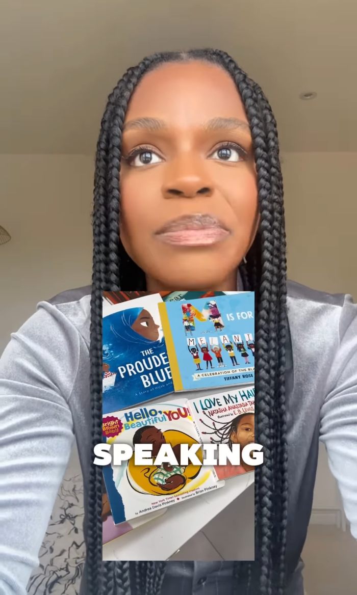Woman with long braided hair holding children's books about Black identity and empowerment, addressing toddler realization at daycare.