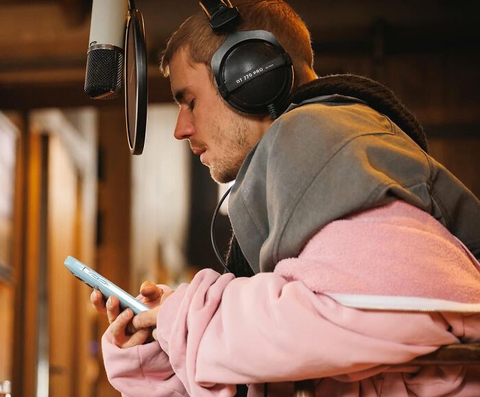 Justin Bieber wearing headphones in a recording studio, focusing on phone while working on new album about marriage and mental struggles.