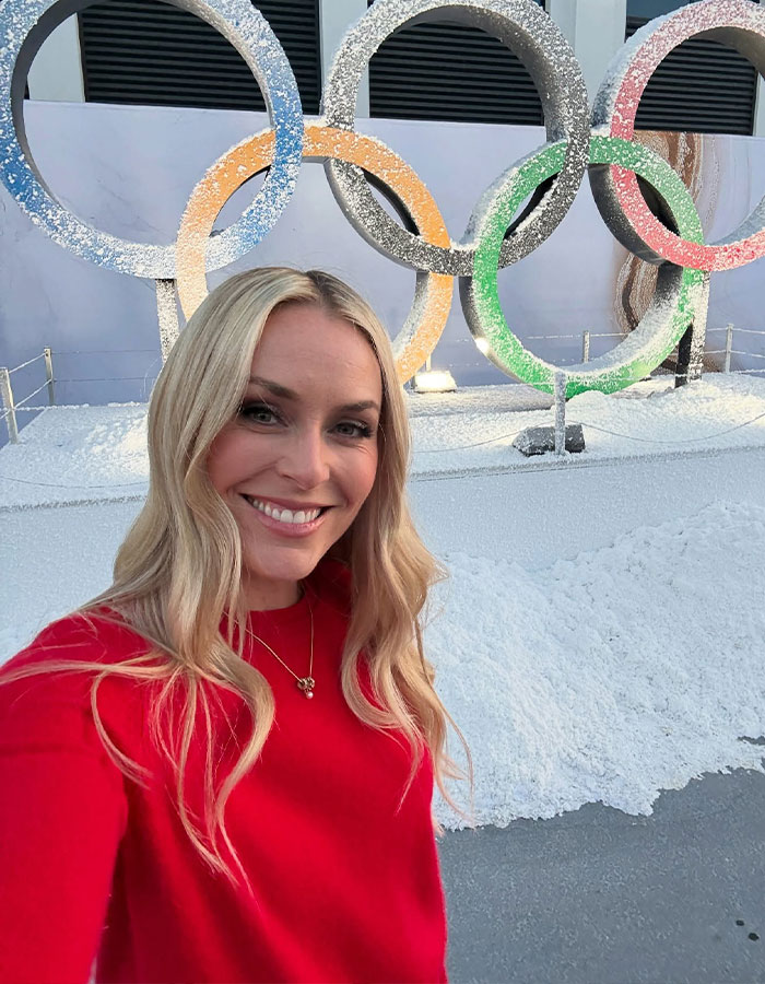 Lindsey Vonn smiling in a red top with Olympic rings in the background at a snowy outdoor location. Lindsey Vonn smiling in a red top with Olympic rings in the background at a snowy outdoor location.