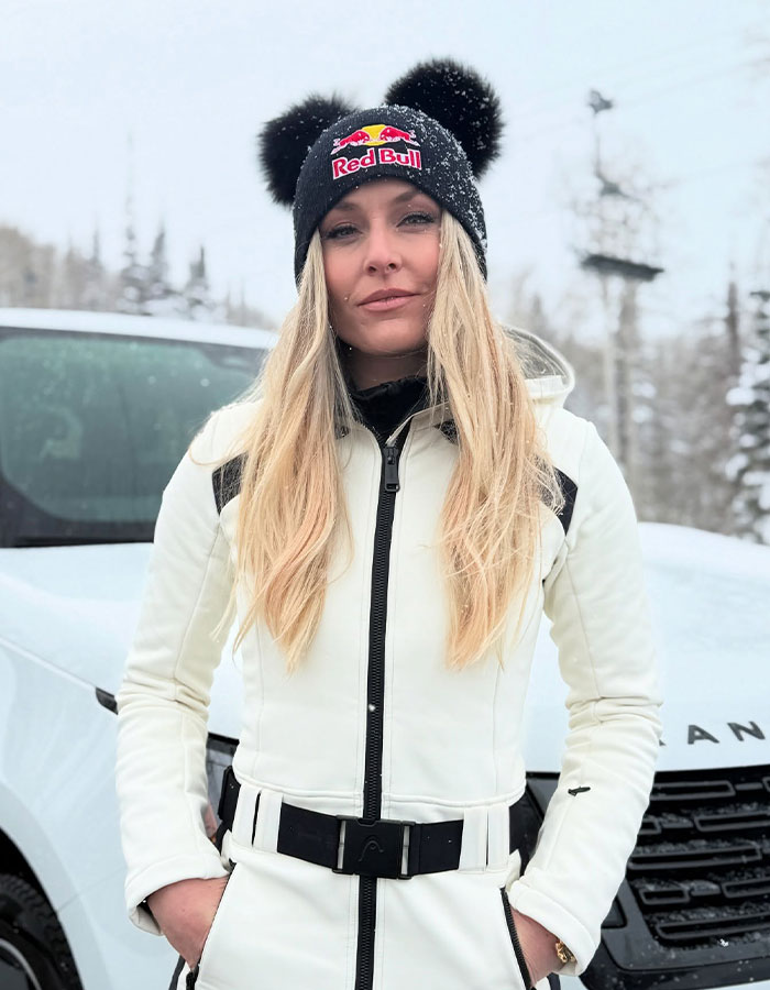 Lindsey Vonn wearing a white jacket and Red Bull beanie outdoors in snowy weather with trees in the background Lindsey Vonn wearing a white jacket and Red Bull beanie outdoors in snowy weather with trees in the background