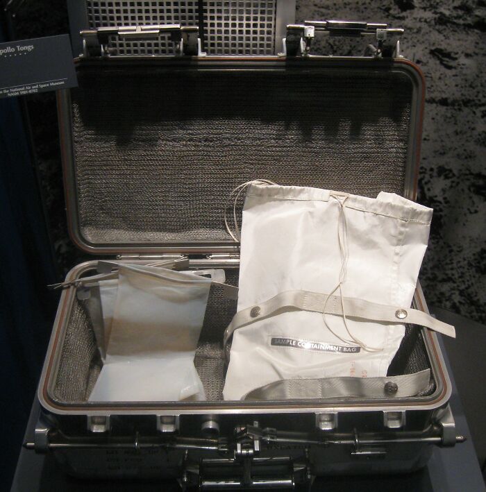 Silver carrying case with white sample containment bags, a high-value collectible item displayed in a museum setting.
