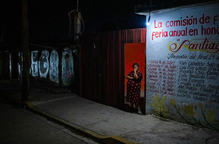 Woman standing in a dimly lit street doorway, capturing honest street moments reflecting everyday life beauty.