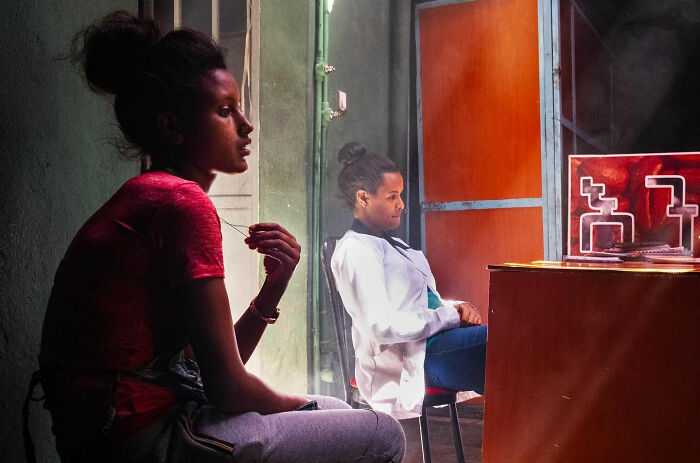 Two people sitting indoors in a candid street moment showing the beauty of everyday life captured by a photographer.