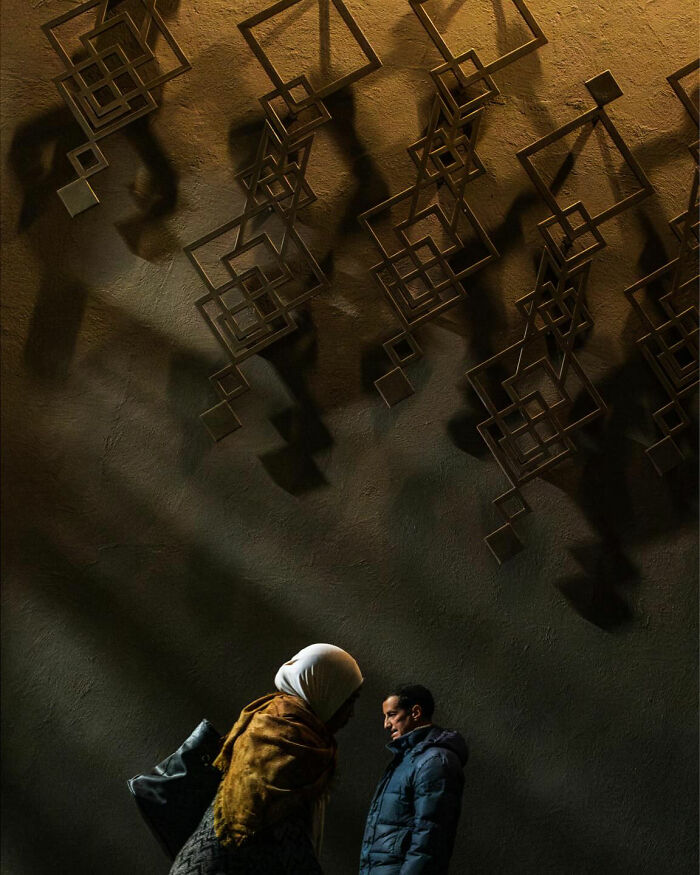 Two people walking under abstract geometric metal art, capturing honest street moments showing the beauty of everyday life.