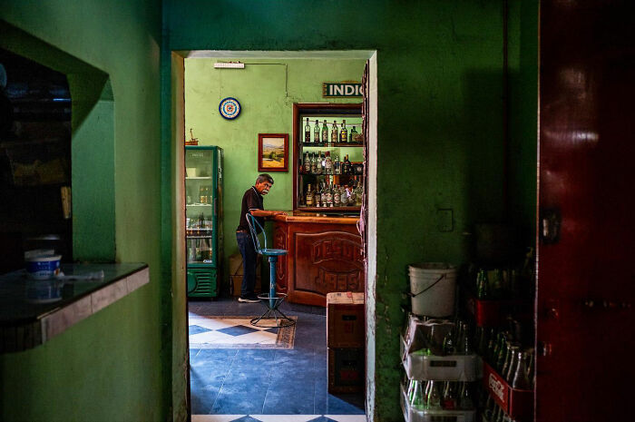 Man standing at a bar counter in a dimly lit room, capturing honest street moments and everyday life beauty.