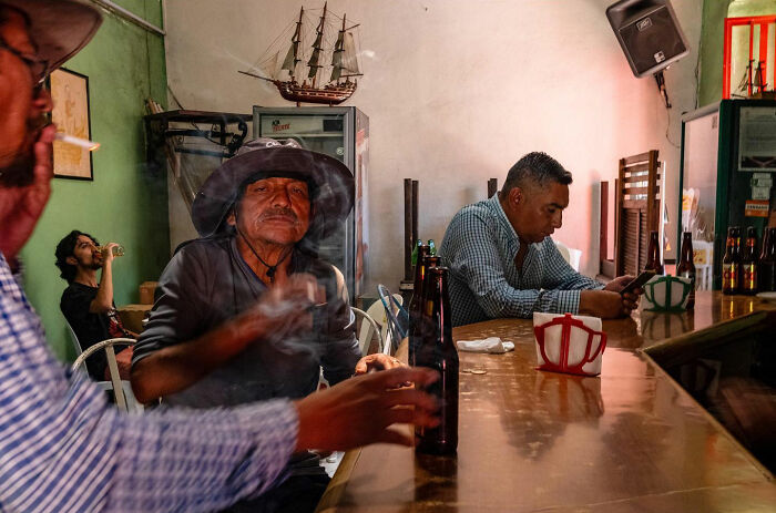 Men enjoying drinks and smoking in a dimly lit bar, capturing honest street moments showing the beauty of everyday life.