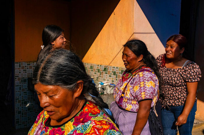 Four women in colorful traditional clothes sharing honest street moments under bright sunlight on a vibrant tiled background.
