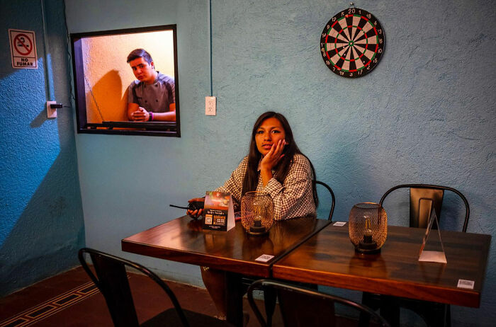 Young woman sitting at a table in a colorful room with a dartboard, capturing honest street moments of everyday life.