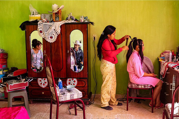 Woman styling another's hair in a colorful room, one of 100 honest street moments capturing the beauty of everyday life.