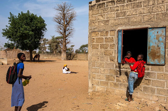 Children interacting near a rustic building in a sunlit rural street, capturing honest street moments and everyday life beauty.