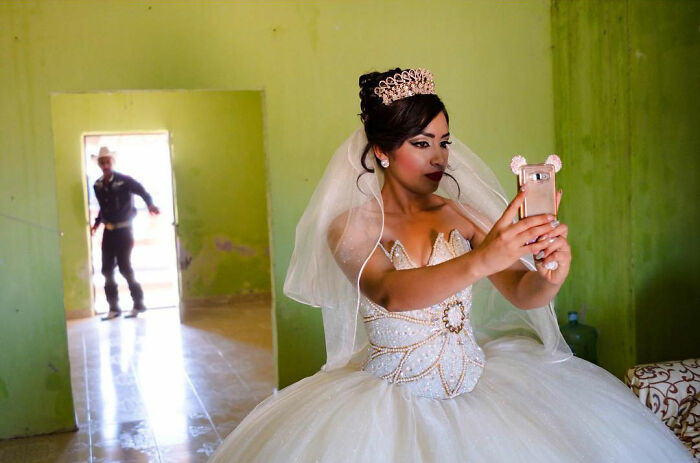 Bride in an elegant dress taking a selfie indoors, capturing an honest street moment that shows everyday life beauty.