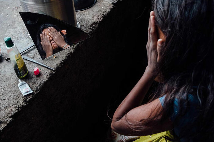Woman covering her face reflected in a broken mirror, capturing honest street moments showing the beauty of everyday life.