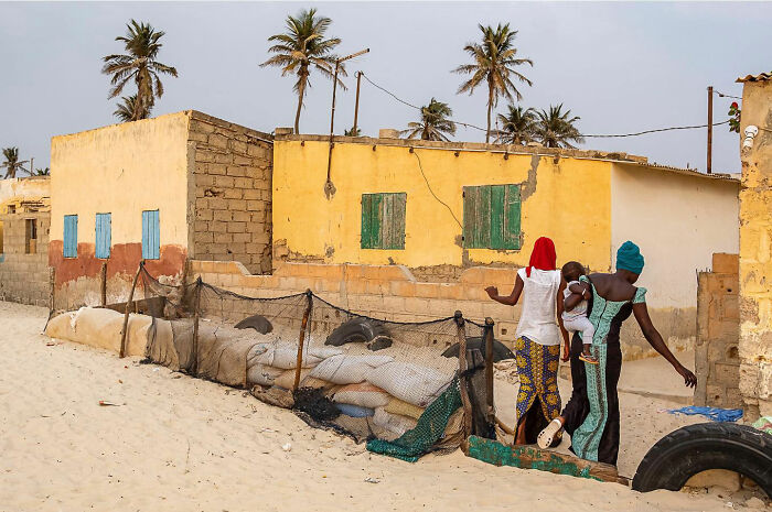 Two women and a child walking through a sandy street in front of colorful houses, capturing honest street moments.