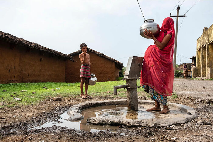 Woman in a red sari and a child at a rural water pump, capturing honest street moments of everyday life.