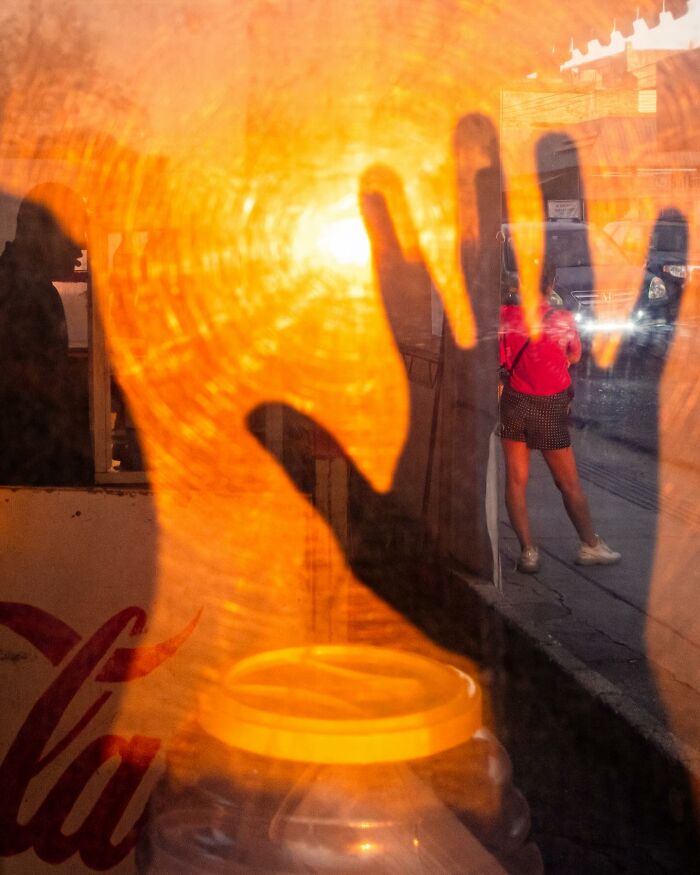 Shadow of hand on glass with a street scene and person in red, capturing an honest street moment of everyday life beauty.