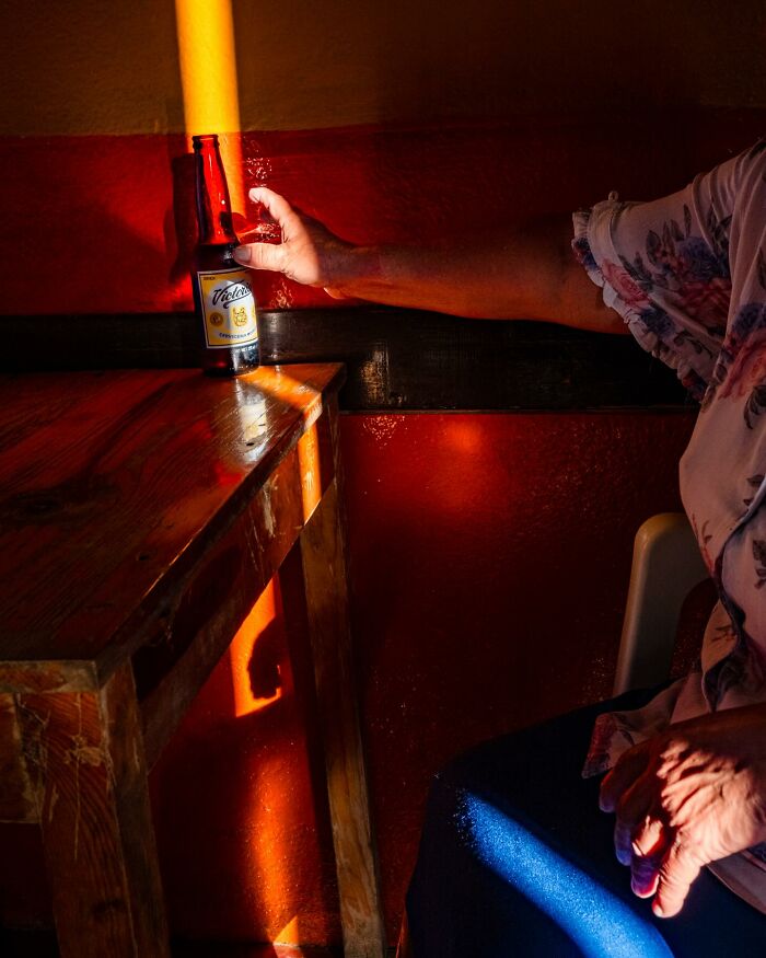 Hand reaching for a bottle on a wooden table in warm light, capturing an honest street moment of everyday life.