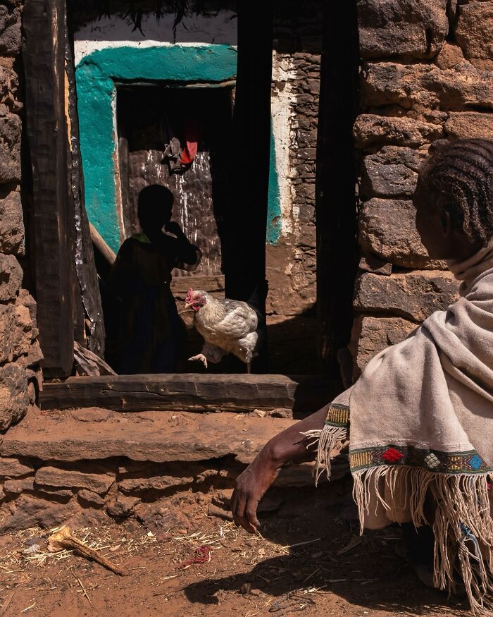 Child in a doorway with a chicken nearby, captured in an honest street moment showing the beauty of everyday life.