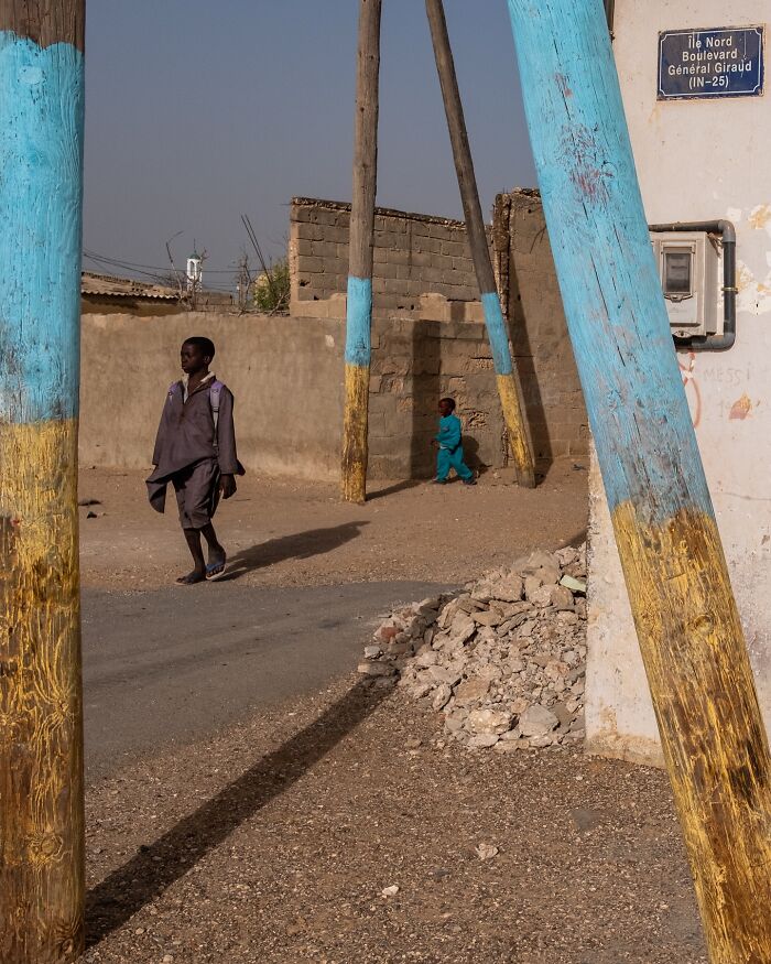 Two children walking near blue and yellow painted poles in a street moment capturing the beauty of everyday life.