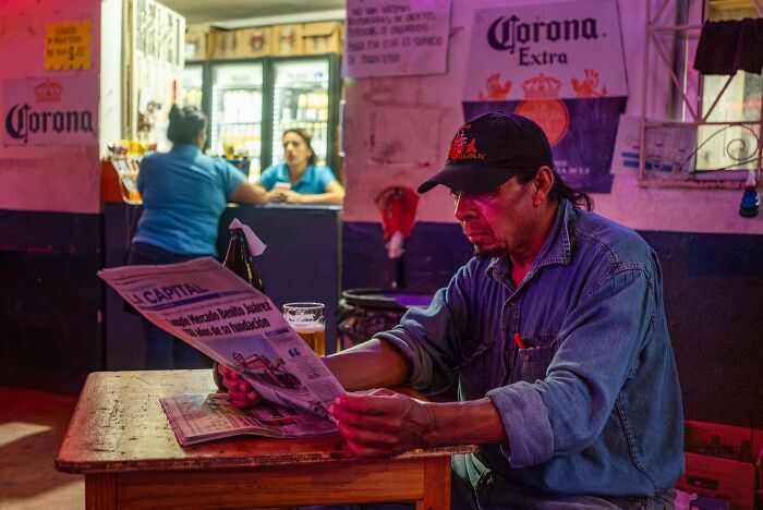Man reading newspaper at bar, captured in an honest street moment showing the beauty of everyday life.