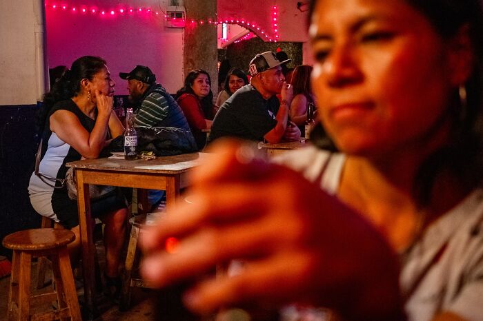 People socializing in a dimly lit room, capturing honest street moments that show the beauty of everyday life.