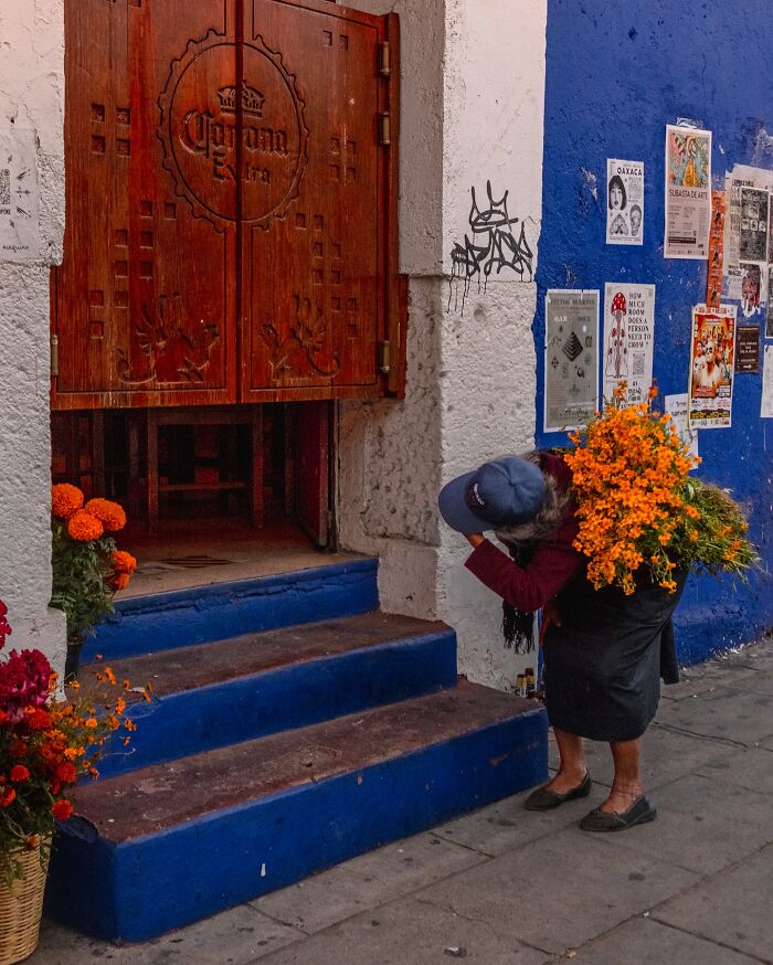 Elderly woman carrying bright orange flowers on street steps, capturing honest street moments and everyday life beauty.