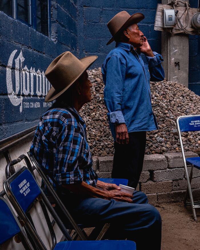 Two men wearing hats in an honest street moment, capturing the beauty of everyday life in a casual setting.