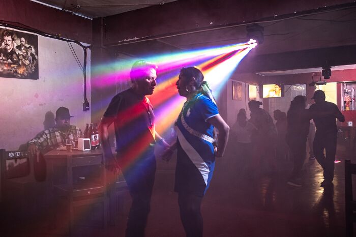 A photographer captured honest street moments showing a couple dancing in colorful light beams inside a dimly lit venue.