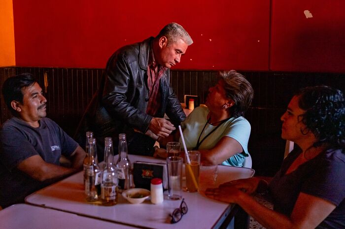 Group of people sharing honest street moments of everyday life at a dimly lit restaurant table with drinks and conversation.