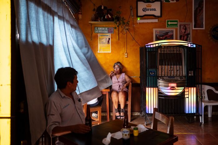 Man sitting at a table with drinks and woman smoking in a colorful room, capturing honest street moments of everyday life.