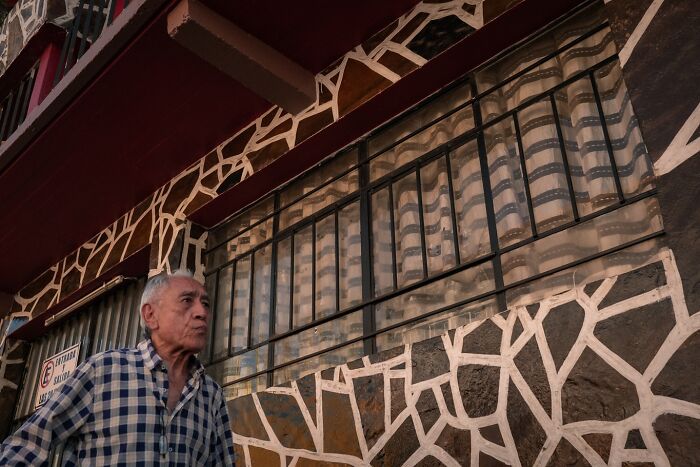 Elderly man walking past a patterned wall, capturing honest street moments showing the beauty of everyday life.