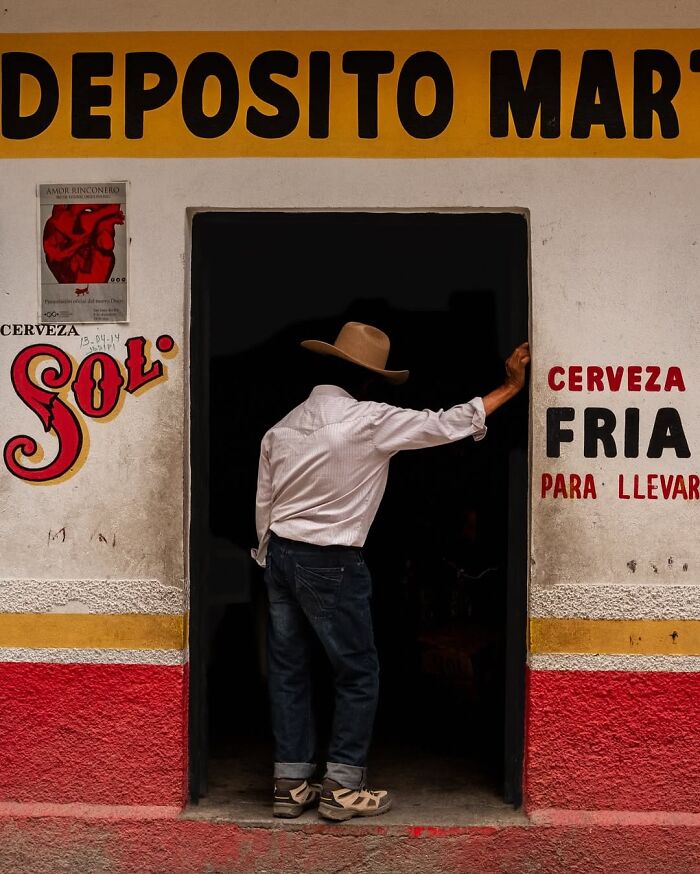 Man in a hat leaning on a doorway, capturing honest street moments that show the beauty of everyday life.