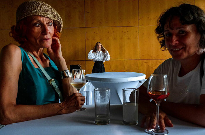 Two women with drinks at a table and a photographer capturing honest street moments showing the beauty of everyday life.
