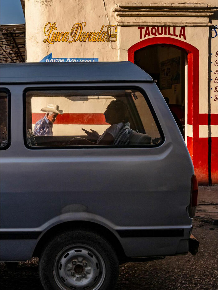 Man in white hat walking outside a building while another person gestures inside a van, showing honest street moments.