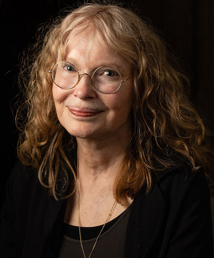 Older woman with curly hair and glasses smiling softly, representing celebrities who criticized Jeff Bezos and Lauren Sánchez wedding.