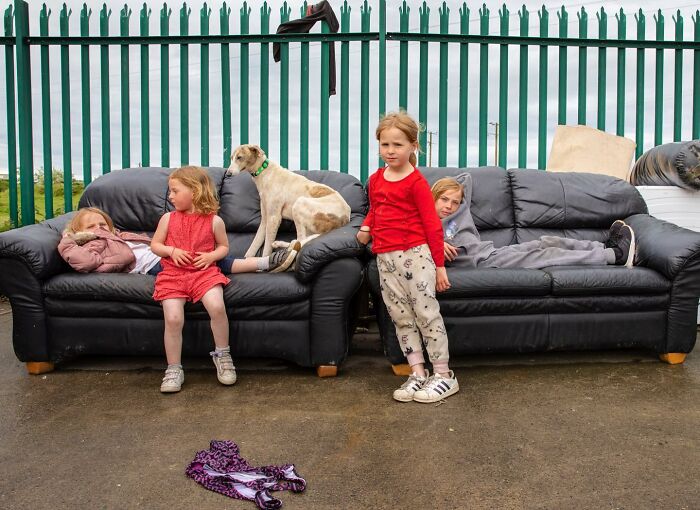 Irish traveller kids sitting and standing on black couches outdoors, growing up with a dog by their side.