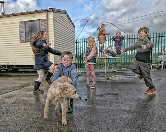 Irish Traveller kids playing outside with a dog and skipping ropes near a caravan on a wet day.