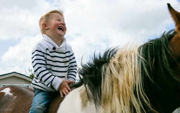 Irish traveller kid laughing while sitting on a horse, enjoying growing up with animals outdoors on a cloudy day