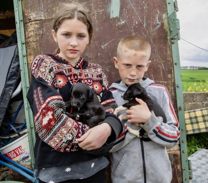 Irish Traveller kids holding black puppies outdoors, showcasing the bond between kids and animals in rural settings.