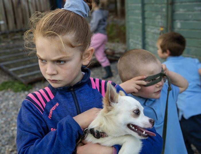 Young Irish Traveller kids growing up with animals, girl holding a small white dog outdoors in casual clothing.
